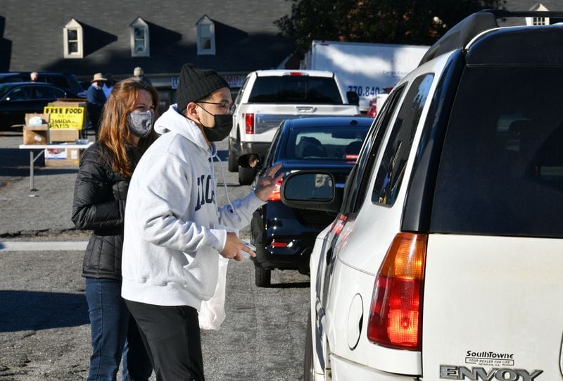January 29, 2021 Norcross - Woojin Kang and Vicki Tyler (left), volunteers from The Nett Church, help patrons, who line up to pick up food and essentials that Chef Hank Reid and volunteers prepared, in the parking lot of The Nett Church in Norcross on Friday, January 29, 2021. Hank Reid has been driving a food truck to bring meals where they are needed in Gwinnett County.  (Hyosub Shin / Hyosub.Shin@ajc.com)