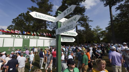 Patrons walk around a sign posting directions to famous areas of interest such as; Amen Corner, with the Masters scoreboard in the background near the first fairway during the practice round of the 2024 Masters Tournament at Augusta National Golf Club, Wednesday, April 10, 2024, in Augusta, Ga. (Jason Getz / jason.getz@ajc.com)