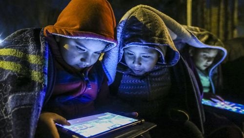 David Lozano, Brandon Martinez and Kimberlyn Lozano (left to right) bundled up and played on their tablets while waiting for their school bus in Brookhaven early Thursday. John Spink / jspink@ajc.com