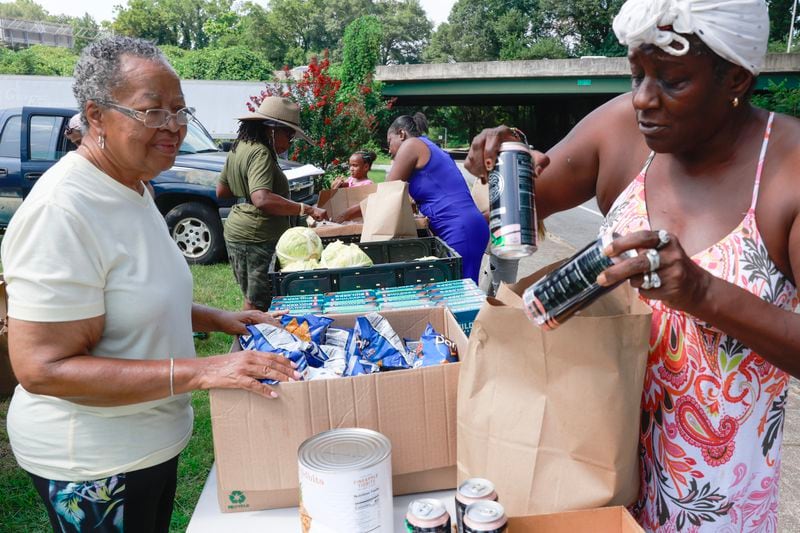 (Left to right) Volunteer Jean Lewis looks on as Tammi Williams fills her bag with free produce and food during the Metro Atlanta Urban Farm food bank held in the West End neighborhood on Tuesday July 25, 2023. (Natrice Miller/natrice.miller@ajc.com)