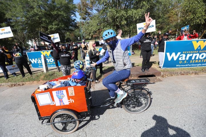 A person riding a bicycle shows a peace sign in front of Raphael Warnock supporters during a rally on election day on Tuesday, Nov. 3, 2020.
Miguel Martinez for The Atlanta Journal-Constitution