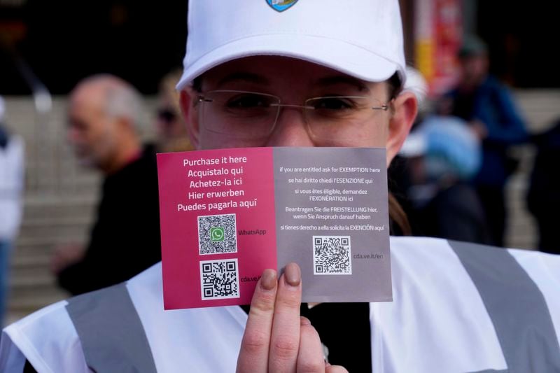 A steward shows the QR code access outside the main train station in Venice, Italy, Thursday, April 25, 2024. The fragile lagoon city of Venice begins a pilot program Thursday to charge daytrippers a 5 euro entry fee that authorities hope will discourage tourists from arriving on peak days. The daytripper tax is being tested on 29 days through July, mostly weekends and holidays starting with Italy's Liberation Day holiday Thursday. Officials expect some 10,000 people will pay the fee to access the city on the first day, downloading a QR code to prove their payment, while another 70,000 will receive exceptions, for example, because they work in Venice or live in the Veneto region. (AP Photo/Luca Bruno)