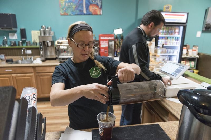 Kasia Jakubowski (center), 46, a barista at Community Grounds Cafe, prepares an iced coffee while Jeff Delp (right), executive director of Carver Neighborhood Market, briefly helps at the register. Community Grounds Cafe is connected to the store and has seen an influx of customers as the variety of products they offer increases. DAVID BARNES / SPECIAL