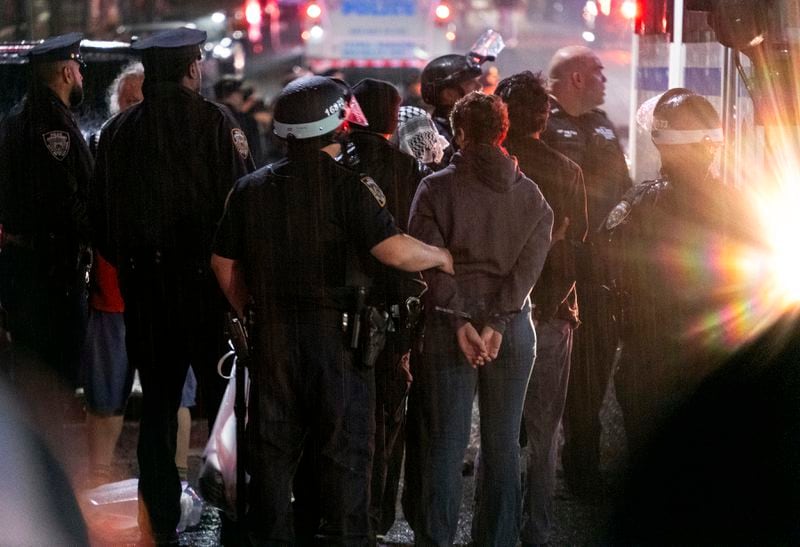 As light rain falls, New York City police officers take people into custody near the Columbia University campus in New York, Tuesday, April 30, 2024, after a building taken over by protesters earlier in the day was cleared, along with a tent encampment. (AP Photo/Craig Ruttle)