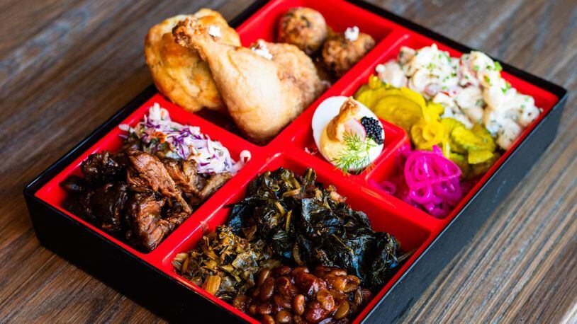 The Southern Bento Box at Watershed rotates with an offering of regional staples. Pictured are a drumstick of the restaurant’s iconic fried chicken, pulled pork, macaroni salad, deviled eggs and collard greens. CONTRIBUTED BY HENRI HOLLIS