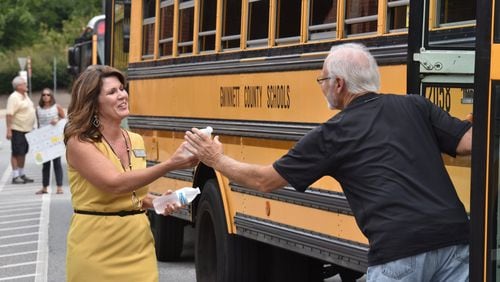 Principal Kim Reed (left) offers a bottle of cold water to a driver as students board buses at Burnette Elementary School in Suwanee on Tuesday, Aug. 13, 2019. With temperatures in the 90s, heat indexes are often in the triple digits when students board school buses for home. Many metro school buses have no air conditioning. (Hyosub Shin / Hyosub.Shin@ajc.com)
