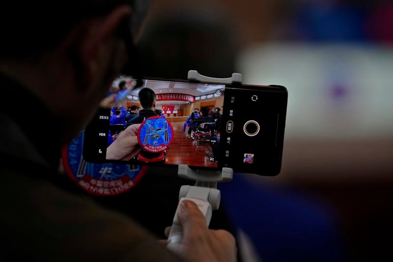 An attendee films a badge depicting the Tiangong space station as Chinese astronauts for the upcoming Shenzhou-18 mission Li Guangsu, Ye Guangfu and Li Cong meet with media members at the Jiuquan Satellite Launch Center in northwest China, Wednesday, April 24, 2024. (AP Photo/Andy Wong)