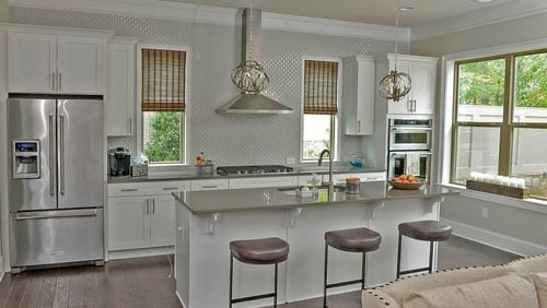 The glossy, white arabesque tile, a custom addition by Harvey, stands out against the stainless steel KitchenAid appliances and Capital Lighting spherical pendants. The hardwood floors are from Shaw.