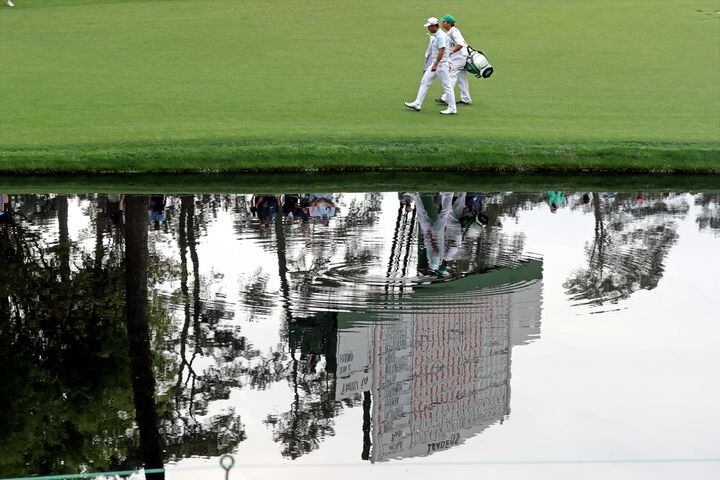 April 10, 2021, Augusta: Hideki Matsuyama and his caddie Shota Hayafuki walk to the sixteenth green with the scoreboard reflected in the pond during the third round of the Masters at Augusta National Golf Club on Saturday, April 10, 2021, in Augusta. Curtis Compton/ccompton@ajc.com