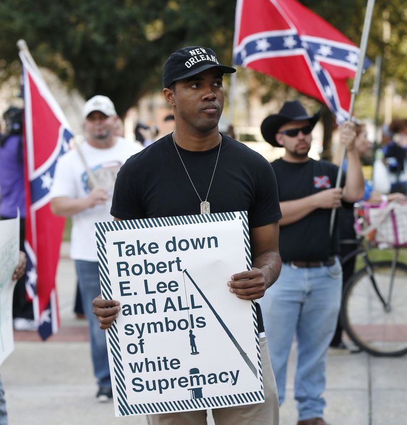 FILE - In this Dec. 10, 2015 file photo, an unidentified participant holds a sign during a rally lead by the Take ‘em Down Coalition, as confederate heritage supporters bear confederate flags nearby in front of City Hall in New Orleans. Backlash has stalled work to remove four Confederate monuments in New Orleans. The backlash has come in the form of lawsuits, boycotts, a possible torching of a contractor’s car, alleged death threats against contractors and protests. Now, a bill in the Louisiana Legislature is taking aim at the removal. (AP Photo/Gerald Herbert, File)