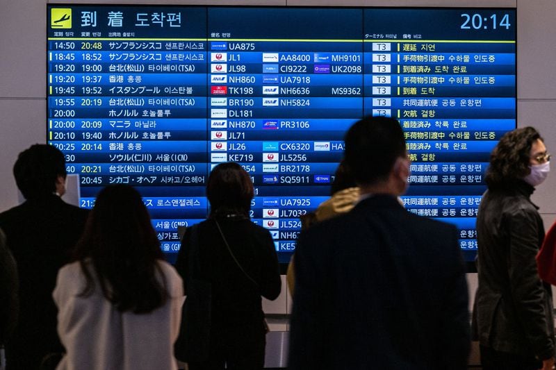 People wait in front a board showing international flight arrivals at Tokyo's Haneda international airport on Wednesday, Dec. 28, 2022.  (Philip Fong/AFP/Getty Images/TNS)