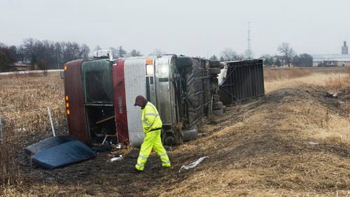 A tow truck operator walks around a bus that flipped over while carrying the Columbus Cottonmouths, a minor-league hockey team. (David Zalaznik/Journal Star via AP)