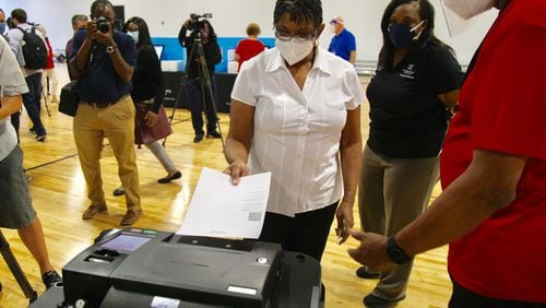 DeKalb County poll worker Deborah Bolden demonstrates part of the voting process during a Friday afternoon press event at CORE4, the Chamblee training facility of former Atlanta Hawks star Paul Millsap, as elections director Erica Hamilton (rear) looks on. CORE4 is one of a dozen early voting venues that will open Monday in DeKalb County.