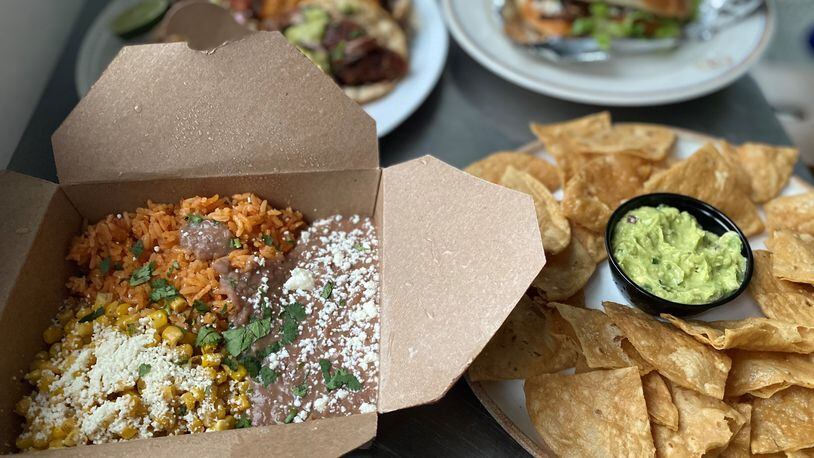 This takeout order from DaniMarco Tacos includes a box of sides (rice, beans and elote); guacamole and chips; and (in the rear) a plate of tacos and a torta with birria. Wendell Brock for The Atlanta Journal-Constitution
