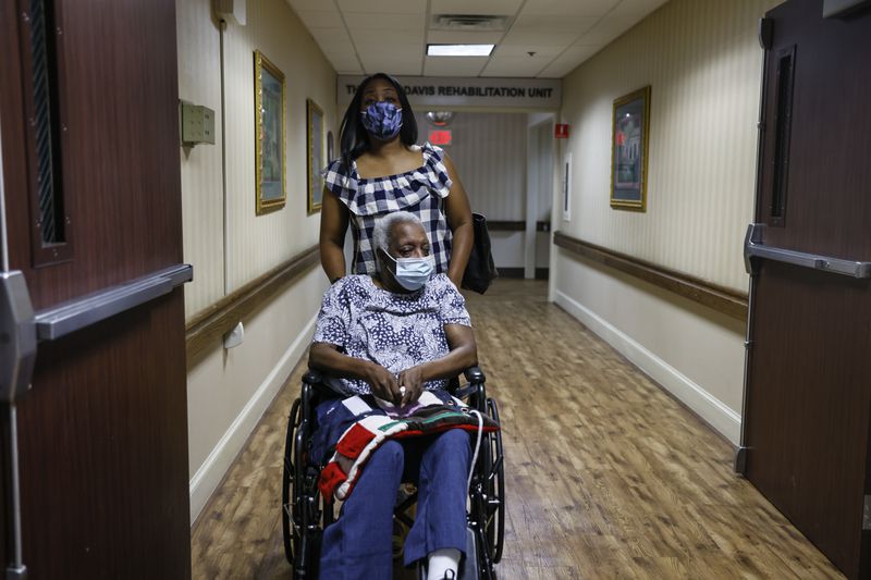 Kisha Stanley pushes her mother, Yvonne Medley, through the hallways of Sandy Springs Center for Nursing and Healing. Medley was previously a resident at Signature HealthCARE of Buckhead, where, Stanley says, showers were scant and her mother developed bed sores. (Natrice Miller / natrice.miller@ajc.com)