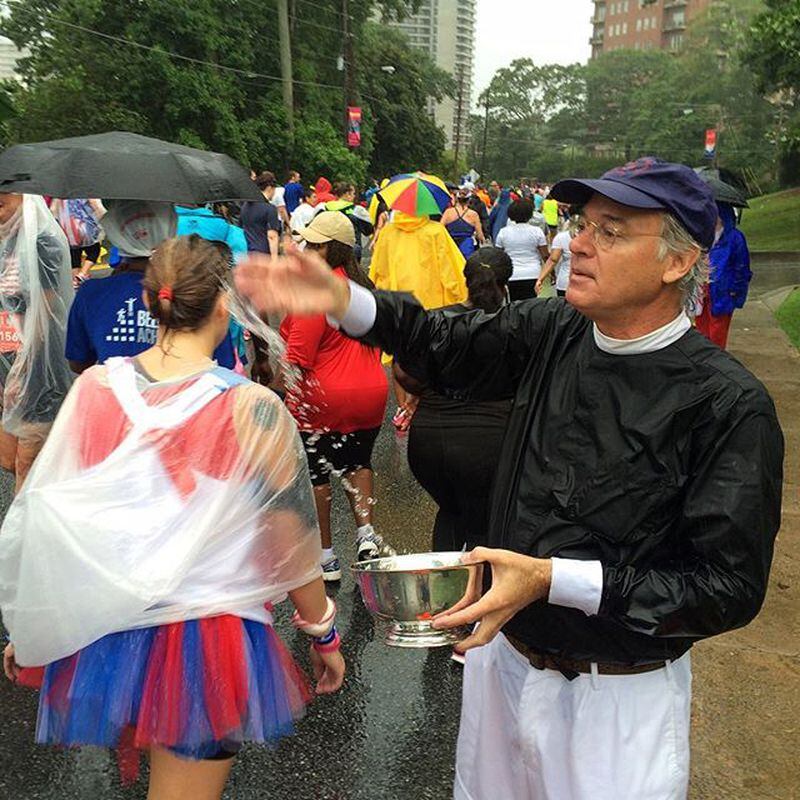 Dean Sam Candler with The Cathedral of St. Philips blesses runners during the 2015 AJC Peachtree Road Race. AJC FILE PHOTO