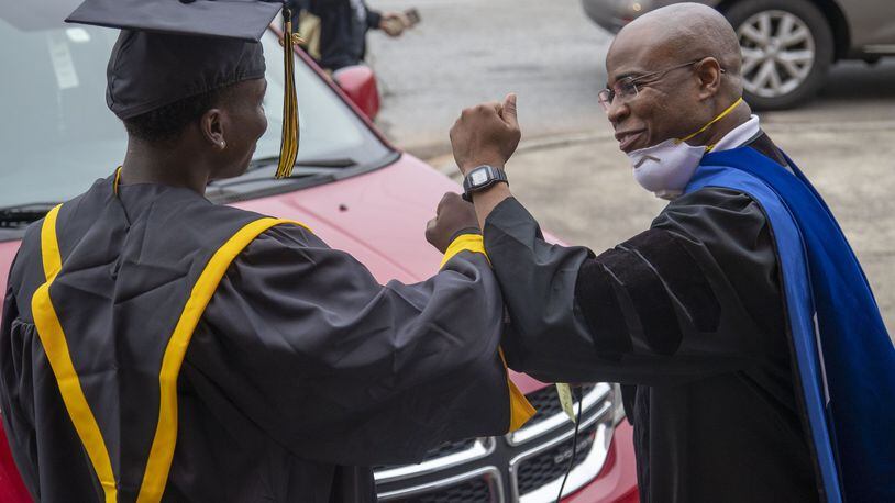 Frederick Douglass High School principal Ellis Duncan (right) congratulates a graduating senior with an elbow bump during a drive-thru celebration event at the school in Atlanta's Center Hill community, Wednesday, May 20, 2020. Graduating seniors were given their diplomas, cap, gowns and academic and athletic awards during the drive-thru event at the school. Students were also given a chance to be photographed win their cap and gown which was provided by the Frederick Douglass High School Alumni Association.