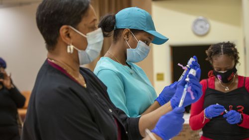 Registered nurses Ashanit Booker, center, and Arnita Dunwell, foreground, prepare the COVID-19 vaccine shot during a DeKalb County Board of Health and Delta Sigma Theta Sorority Inc. COVID-19 vaccination event at the Lou Walker Senior Center in Stonecrest. (Alyssa Pointer / Alyssa.Pointer@ajc.com)