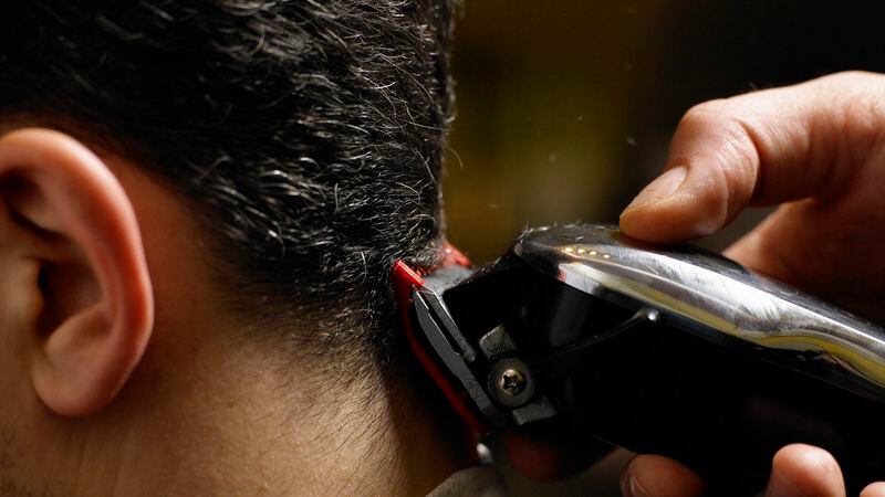 Barber cutting man's hair, close-up of electric razor, side view