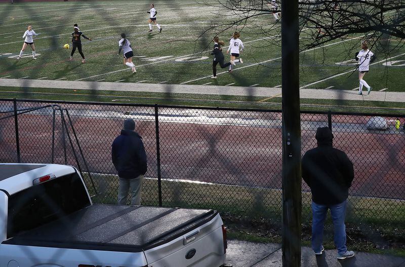 Parents watch their daughters compete in the girls soccer game from the sidewalk outside the fence on Chester Avenue at Maynard Jackson High School on Feb. 18, 2021, in Atlanta. Atlanta Public Schools isn’t allowing parents or any spectators to watch athletic events in-person because of COVID-19. (Curtis Compton / Curtis.Compton@ajc.com)
