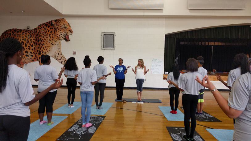 May 18, Atlanta: Cheryl Crawford ( center right), of Grounded Kids Yoga, leads Sandtown Middle School students in yoga with P.E. teacher Tracy Baker (next to her in blue shirt), a former science teacher who will be teaching yoga full-time at the school in the fall after earning her yoga teaching credential from Crawford. This session at the Fulton County school's gym was a practice run.