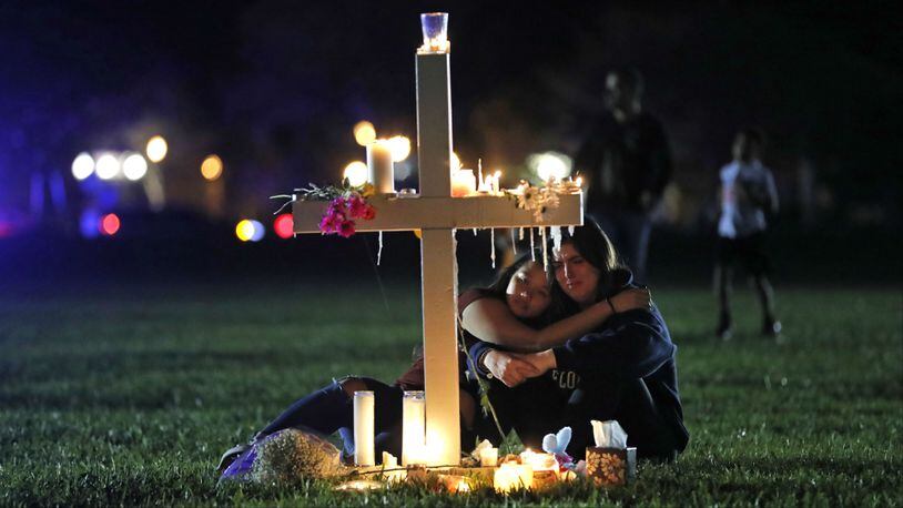 Mourners comfort each other as they sit at one of 17 crosses following a candlelight vigil the day after the Valentine's Day massacre at Marjory Stoneman Douglas High School, in Parkland, Florida.