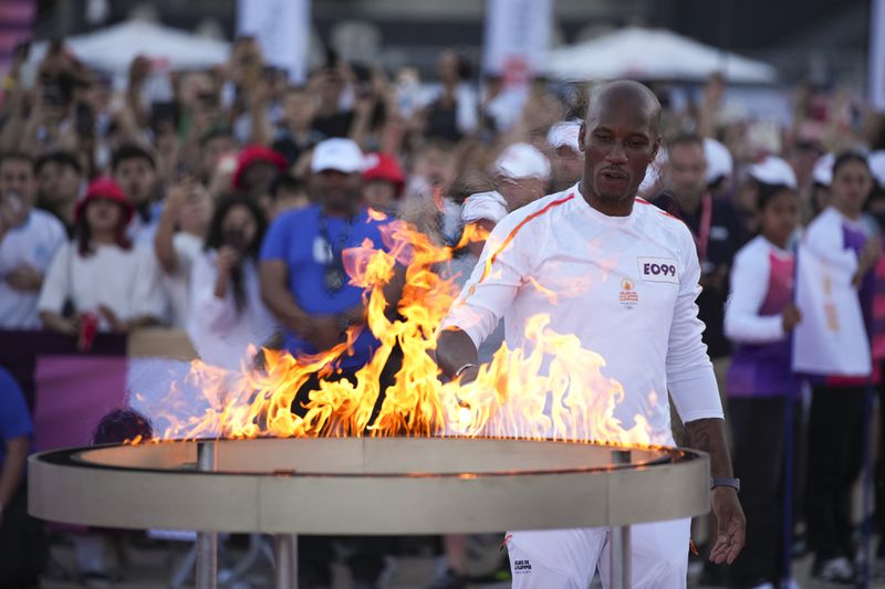 Torchbearer Didier Drogba of France holds the Olympic torch to light the cauldron at the Velodrome stadium in Marseille, southern France, Thursday, May 9, 2024. Torchbearers are to carry the Olympic flame through the streets of France's southern port city of Marseille, one day after it arrived on a majestic three-mast ship for the welcoming ceremony. (AP Photo/Daniel Cole)