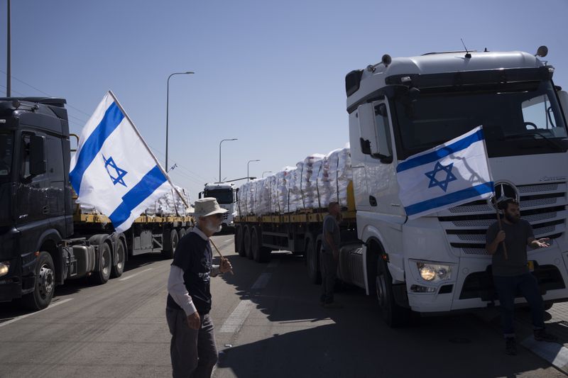 Holding Israeli flags people stand in front of trucks carrying humanitarian aid as they try to stop them to enter in the Gaza Strip in an area near the Kerem Shalom border crossing between Israel and Gaza, in southern Israel, in Kerem Shalom, Thursday, May 9, 2024. (AP Photo/Leo Correa)