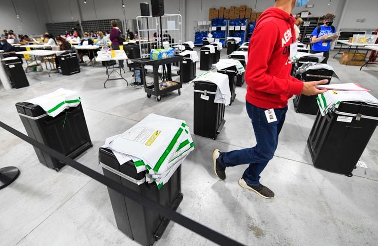 A worker walks past cases of ballots yet to be counted during the Presidential recount of votes at the Gwinnett County elections office on Friday, Nov.13, 2020 in Lawrenceville. (JOHN AMIS FOR THE ATLANTA JOURNAL-CONSTITUTION)