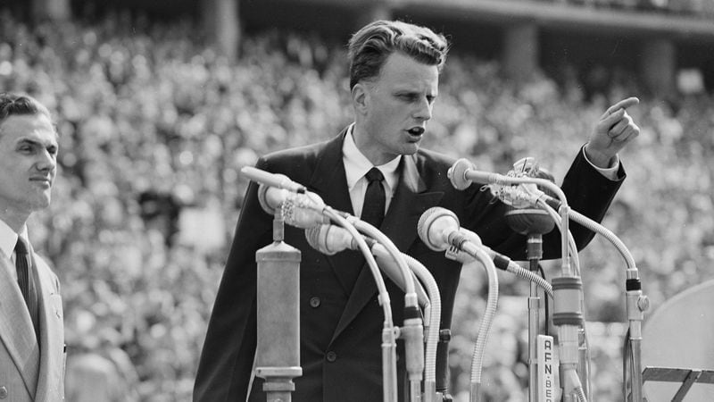 FILE - In this June 27, 1954 file photo, Evangelist Billy Graham speaks to over 100,000 Berliners at the Olympic Stadium in Berlin, Germany.   Graham, who transformed American religious life through his preaching and activism, becoming a counselor to presidents and the most widely heard Christian evangelist in history, has died. Spokesman Mark DeMoss says Graham, who long suffered from cancer, pneumonia and other ailments, died at his home in North Carolina on Wednesday, Feb. 21, 2018. He was 99. (AP Photo, File)