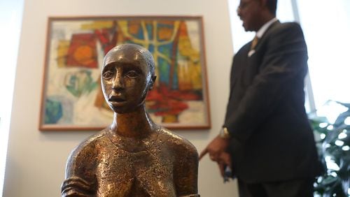 Atlanta Life President Geoffrey Nnadi looks over a painting in his office behind the bronze sculpture Pensive by Elizabeth Catlett at the firm's downtown offices in June. Since Atlanta Life moved from Auburn Avenue to a skyscraper on Peachtree Street, its vast collection of African-American art has become inaccessible to the public. Curtis Compton / ccompton@ajc.com