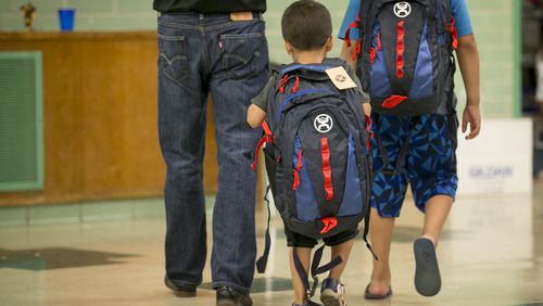 Adrien Sosa, 4, middle, and his brother Eric Sosa, 8, walk away with new backpacks filled with new clothes and books  at the Manos de Cristo Back-to-School Program at the Allan Early Childhood Center on Tuesday July 25, 2017.  The nonprofit Manos de Cristo is providing the school supplies and clothes to children, aged pre-K to 5th grade, every morning this week.   Hundreds of volunteers, including board member Paul Miller, left, will serve 2,000 children with  supplies which were donated by corporate sponsors and individuals.  JAY JANNER / AMERICAN-STATESMAN