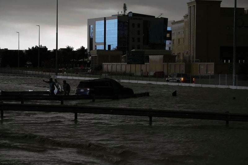 Men gesture as they try to tow a vehicle out of standing water in Dubai, United Arab Emirates, Tuesday, April 16, 2024. Heavy rains lashed the United Arab Emirates on Tuesday, flooding out portions of major highways and leaving vehicles abandoned on roadways across Dubai. Meanwhile, the death toll in separate heavy flooding in neighboring Oman rose to 18 with others still missing as the sultanate prepared for the storm. (AP Photo/Jon Gambrell)