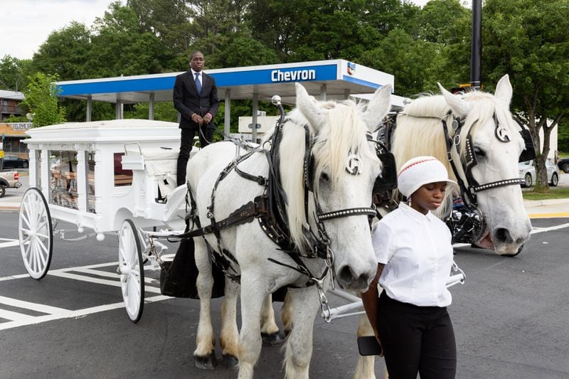 A horse and carriage pulling the carrying the casket of hip-hop pioneer Rico Wade stops at the intersection of Headland and Delowe, an hip-hop landmark in East Point, on Friday, April 26, 2024. (Arvin Temkar / AJC)