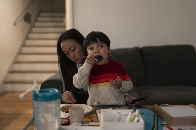 Ethan Quinn, 4, watches a YouTube video while eating dinner with help from his mother, I-Ting, in Concord, Calif., Wednesday, Nov. 1, 2023. A year before Quinn's son was old enough for kindergarten, she and her husband had the option to enroll him in “transitional kindergarten” — a program offered for free by California elementary schools for some 4-year-olds. Instead, they kept Ethan in a private daycare center in Concord at a cost of $400 a week. (AP Photo/Jae C. Hong)