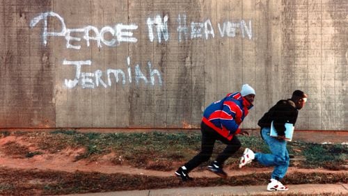 On Nov. 11, 1991, youths ran past a hastily painted sign in the Summerhill-area housing housing project where Jeremiah Anderson was gunned down at a street craps game early Sunday morning. (AJC file photo)