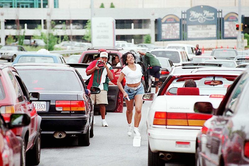 A woman runs back to her car after posing quickly for another Freaknik participant near Phipps Plaza and Lenox Mal.l After the malls closed traffic came to a standstill on Peachtree and Lenox Roads during the 1995 gathering.