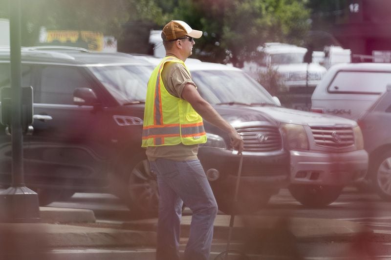 6/19/2019 — Marietta, Georgia — An undercover Marietta Police officer stands in a median looking for distracted along US 41 during a multi-agency distracted driving enforcement operation in Marietta, Wednesday, June 19, 2019. The operation, which involved three under-cover Marietta Police officers dressed as construction workers, took place at the intersection of US 41 and Roswell Road. When the officers saw a distracted driving violation, in addition to others, they radioed ahead and one of the forty officers involved in the operation issued a citation to the driver. (Alyssa Pointer/alyssa.pointer@ajc.com)