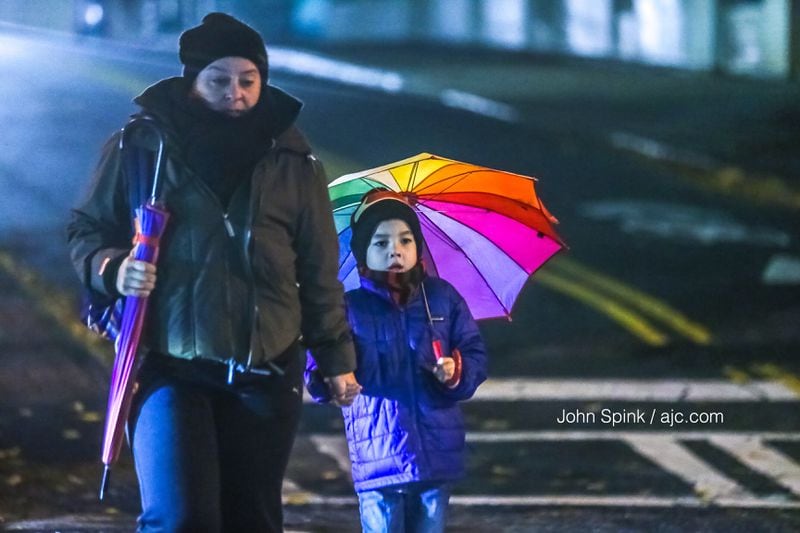 Tatina Williams walks her son Leonardo, 6, across the intersection of 8th and Peachtree streets in the rain Friday morning. JOHN SPINK / JSPINK@AJC.COM