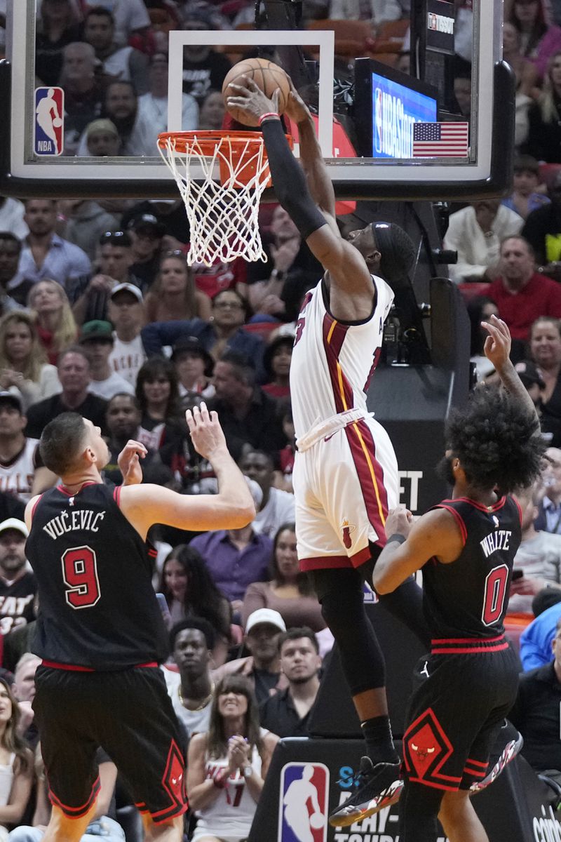 Miami Heat center Bam Adebayo (13) dunks the ball against Chicago Bulls center Nikola Vucevic (9) and guard Coby White (0) during the second half of an NBA basketball play-in tournament game, Friday, April 19, 2024, in Miami. (AP Photo/Wilfredo Lee)