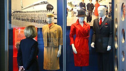 At the Delta Flight Museum, flight crew member Karen Januszewski takes in a display of designer uniforms including a 1959 accessorized uniform with "Jet flame" ascot scarf that were designed by Academy Award-winning Paramount Pictures chief designer Edith Head (at left) and today's flight attendant uniforms of iconic red dresses and navy blue pieces designed by Richard Tyler in 2006. CURTIS COMPTON / CCOMPTON@AJC.COM