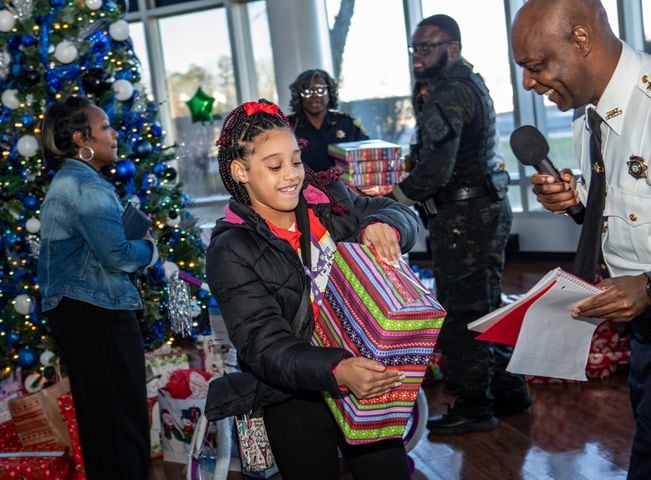 DeKalb County Sheriff’s Office holds the 16th annual Adopt-A-Family celebration on Tuesday, Dec 16, 2023 where Layla Watkins,10, opens her first gift at the party. Law enforcement officers donate their own money and buy gifts for about a dozen local children.  (Jenni Girtman for The Atlanta Journal-Constitution)