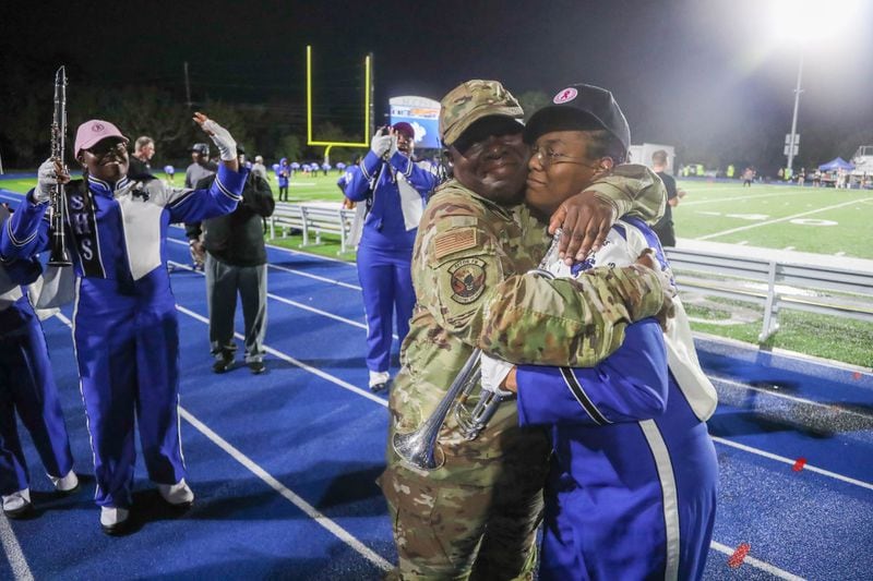 The Savannah High Marching Band cheers as Chief Master Sergeant Alicia Stewart of the 165th Airlift Wing, gives her daughter Alayna Duke a big hug after surprising her following the Band's halftime performance on Friday, October 13, 2023 at Savannah High Stadium. Stewart has been deployed for the past 6 months and just returned home to surprise her daughter at the game.