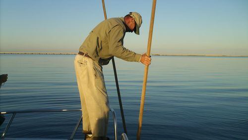 An oysterman works his oyster tongs in Apalachicola Bay near St. George Island. In the distance is the five-mile long bridge that connects the island to the mainland. Credit: Blake Guthrie