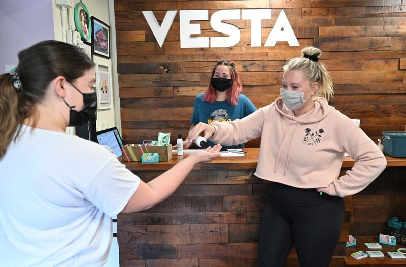 Alixx Hetzel (right) co-owner, offers a gym member Kelsey Cortez (left) a hand sanitizer as she checks in at VESTA Movement Ponce in Atlanta on Wednesday. (Hyosub Shin / Hyosub.Shin@ajc.com)