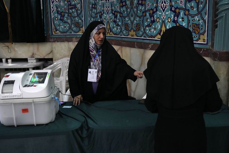 A staff member at a polling station speaks with a voter during the parliamentary runoff elections, in Tehran, Iran, Friday, May 10, 2024. Iranians voted Friday in a runoff election for the remaining seats in the country's parliament after hard-line politicians dominated March balloting. (AP Photo/Vahid Salemi)