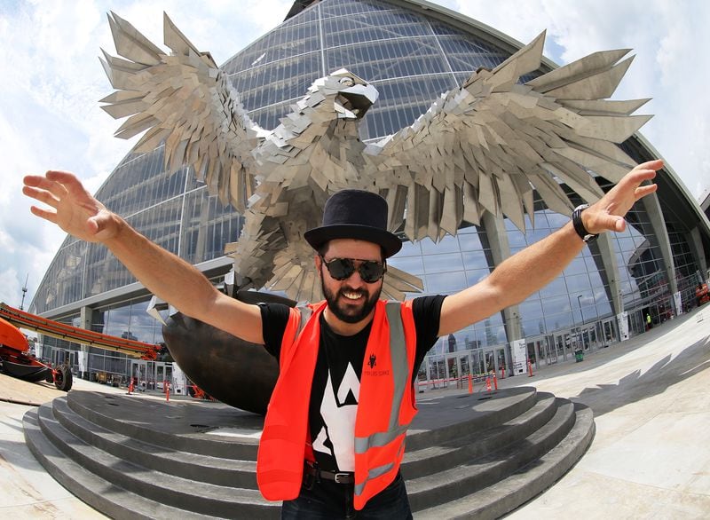 Artist Gabor MIklos Szoke strikes a pose with his stainless steel sculpture of a falcon that is 41.5 feet tall and has a wingspan of more than 64 feet during a tour of Mercedes-Benz Stadium on Thursday, June 1, 2017, in Atlanta.     Curtis Compton/ccompton@ajc.com