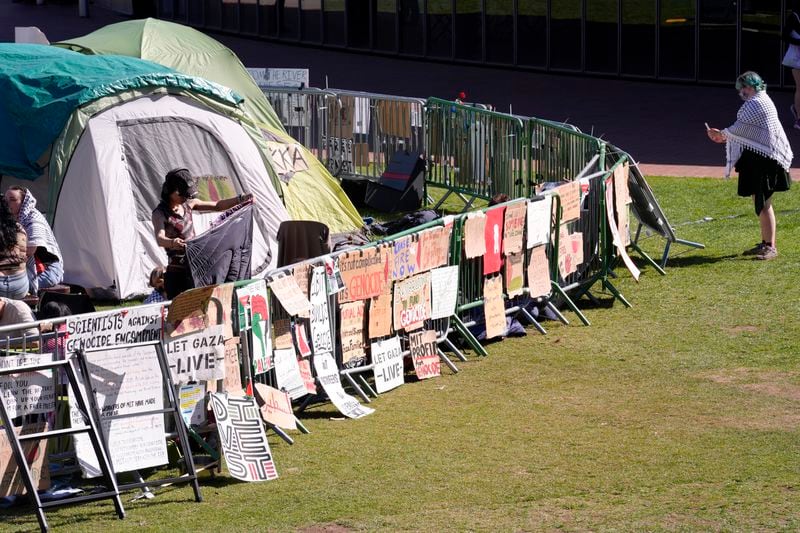 A passer-by, right, uses a mobile device to record a barrier with placards at an pro-Palestinian encampment of tents on the campus of Massachusetts Institute of Technology, Tuesday, May 7, 2024, in Cambridge, Mass. Students at MIT set up the encampment to protest what they said was MIT's failure to call for an immediate ceasefire in Gaza and to cut ties to Israel's military. (AP Photo/Steven Senne)