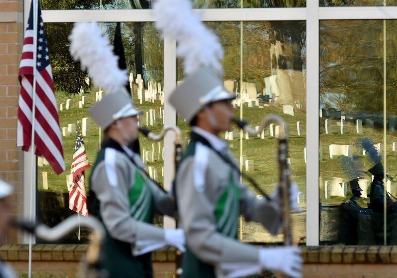 VETERAN REFLECTION--November 11, 2015 Marietta, GA: Tombstones from the Marietta National Cemetery are reflected in a store window as a marching band passes during the annual Marietta Veterans Day Parade Wednesday November 11, 2015. The parade started at Roswell Street Baptist Church and concluded with a ceremony at the Marietta Square. More than 30 parade entries took part in the event including marching bands from Cobb County and Marietta Schools, military vehicles, and various veterans organizations. BRANT SANDERLIN/BSANDERLIN@AJC.COM