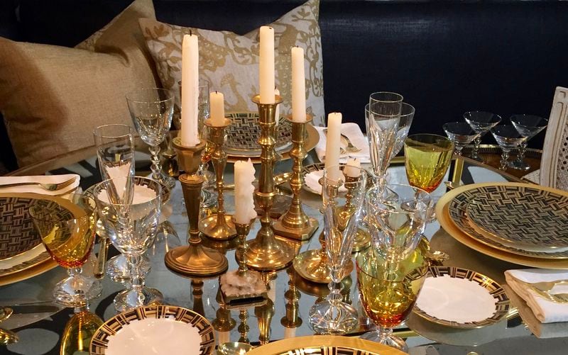 Various brass candle holders with candles of different height arranged to create an opulent centerpiece that complements the gold china and amber-tone glassware.